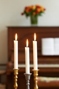tre candele accese di fronte a un painoforte con sopra dei fiori in vaso in vetro