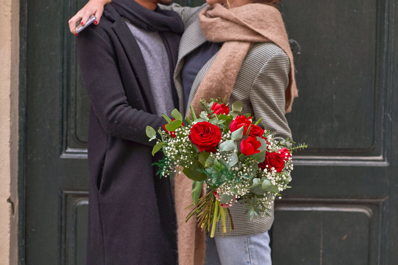ragazza che tiene in mano un bouquet di fiori rossi e verdi mentre abbraccia un ragazzo