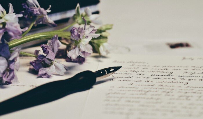 penna che scrive un messaggio per San Valentino con fiori a fianco