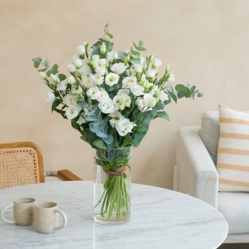 bouquet di lisianthus bianchi all'interno di un vaso trasparente sopra un tavolo in marmo e decorati con elementi naturali verdi