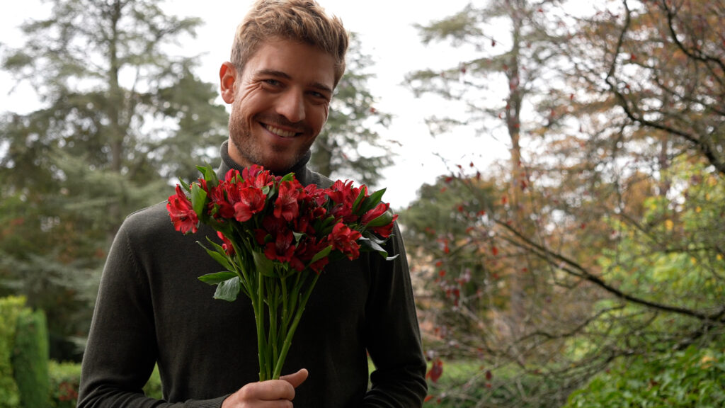 Ragazzo che tiene in mano un bouquet di alstroemerie rosse.