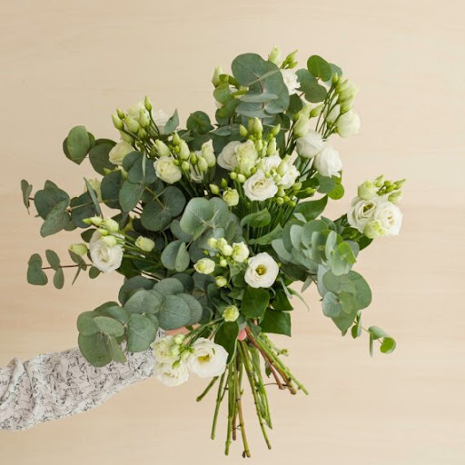 bouquet di lisianthus bianchi tenuti da una mano e decorati con elementi naturali verdi
