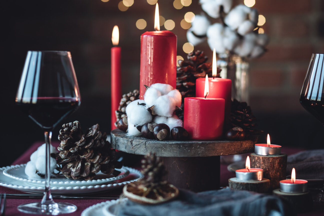 centrotavola di Natale con elementi moderni, candele rosse, pigne e legno nero
