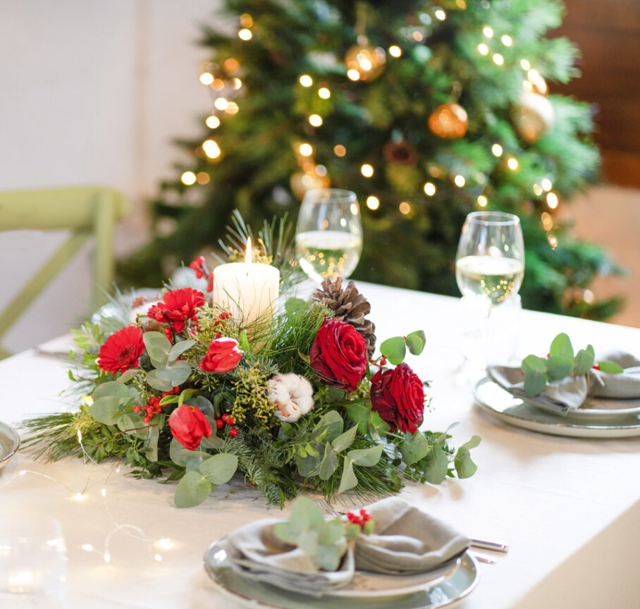 Centrotavola di Natale elegante con al centro una candela bianca in mezzo a un bouquet di rose e tulipani rossi, fiori bianchi e del verde.