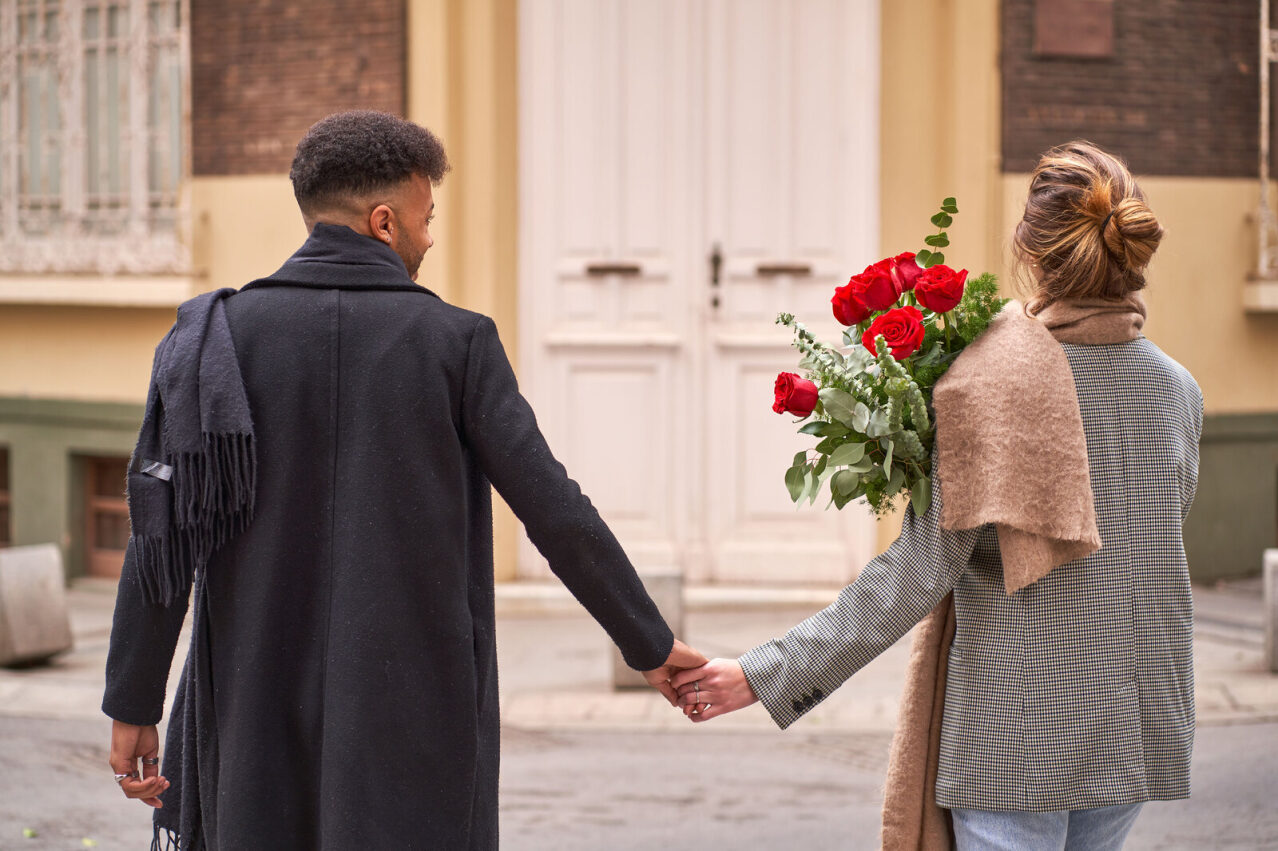 Un ragazzo e una ragazza si tengono per mano mentre lei tiene un bouquet di fiori