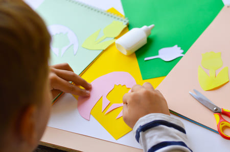 bambino che incolla fiori finti ritagliati in un biglietto per ringraziare la maestra