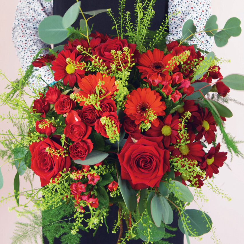 fiori rossi, rose e tulipani in un bouquet con foglie verdi tenuto in mano dal nostro fiorista Interflora