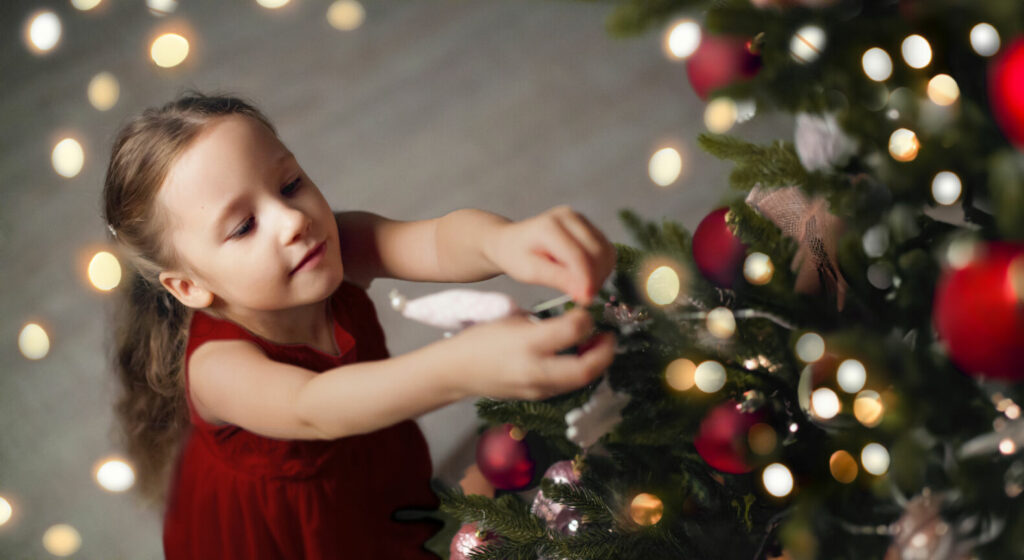 bambina che decora un albero di natale seguendo le tendenze del 2023